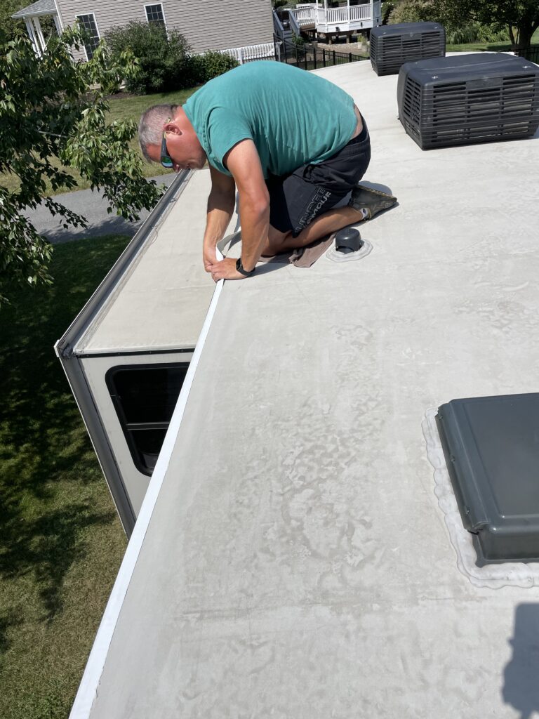 Man on RV roof as he applies tape to seal corner edge of roof